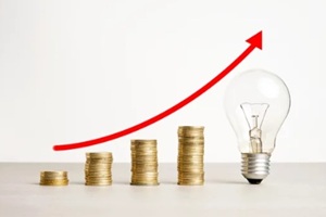 image of increasing stacked coins a transparent light bulb with a rising red arrow above it on a neutral background
