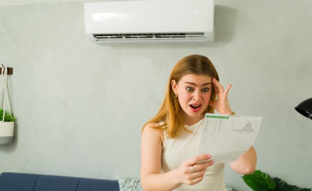 shocked Maryland homeowner holding electricity bill under air conditioner unit