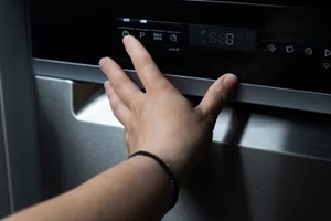 hand selecting dishwasher program on control panel