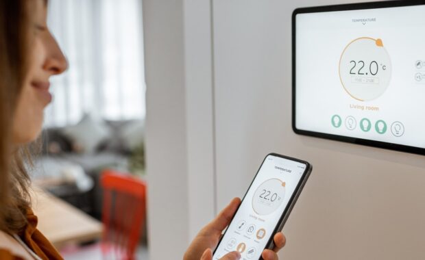 young woman controlling temperature in the living room with smart phone and digital touch screen panel