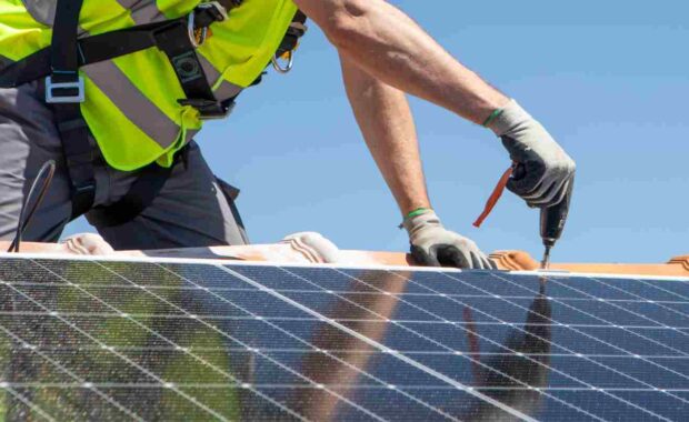 Worker Installing Solar Panel with Drill Machine on Rooftop
