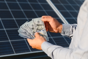 Person Counting Dollars Near Solar Panels Reperesenting Energy Bill Saving